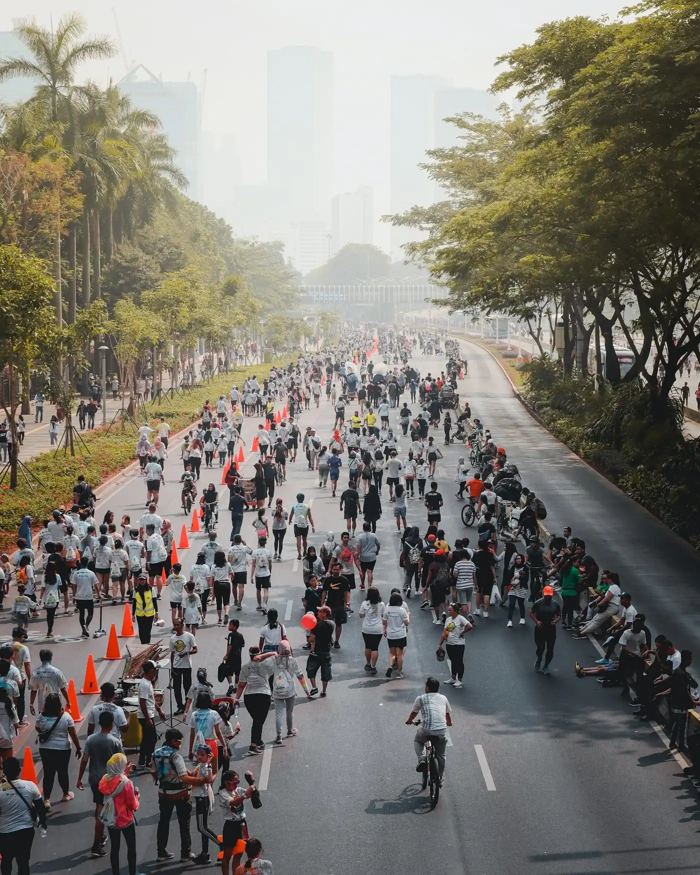 A long Jakarta street full of people walking during car-free day, towers in the haze